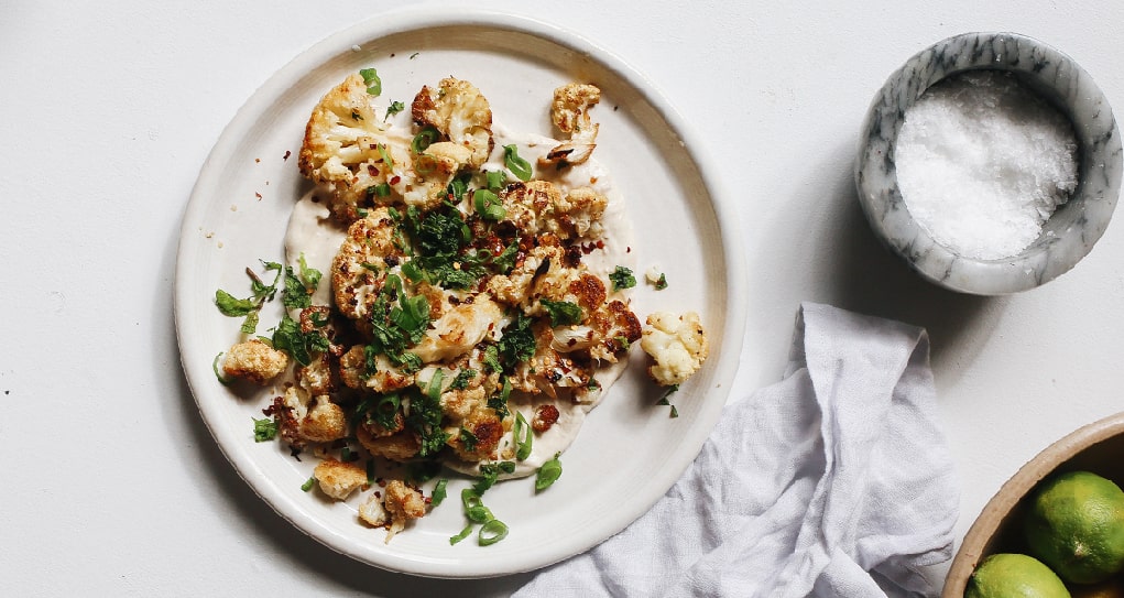 Whole roasted cauliflower drizzled with tahini sauce and herbs