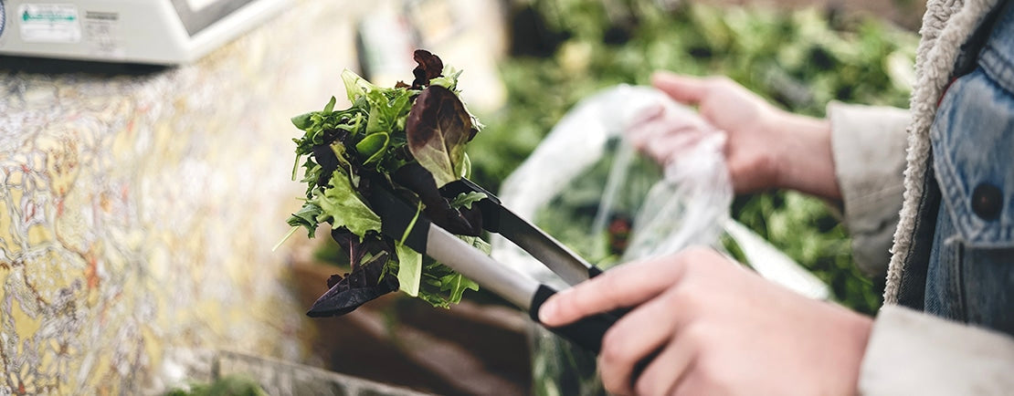 Close up of someone putting lettuce into a bag at a farmer's market.