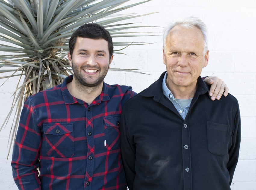 Two men standing together with a plant in the background