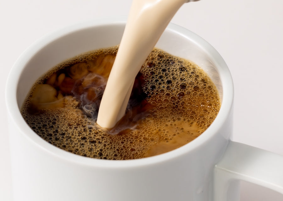 White cup with coffee being poured, showing a close-up of the foam.
