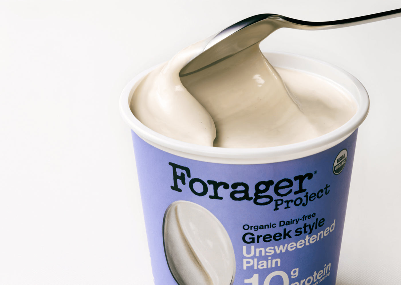 Forager Project Greek style yogurt with a spoon lifting some out of the container.