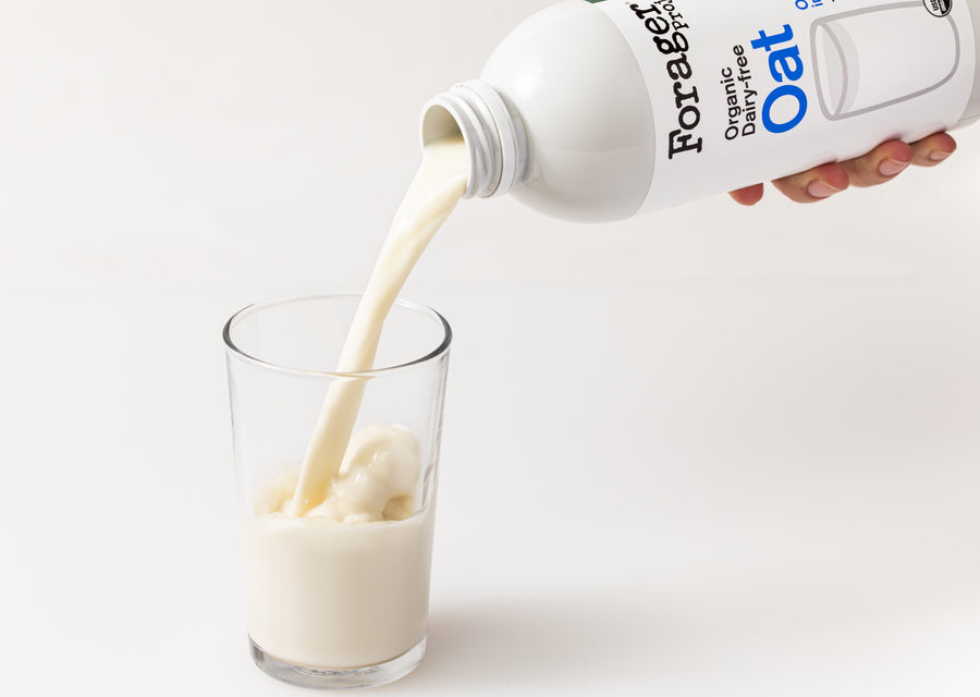 Hand pouring Forager Oat milk into a glass on a white background