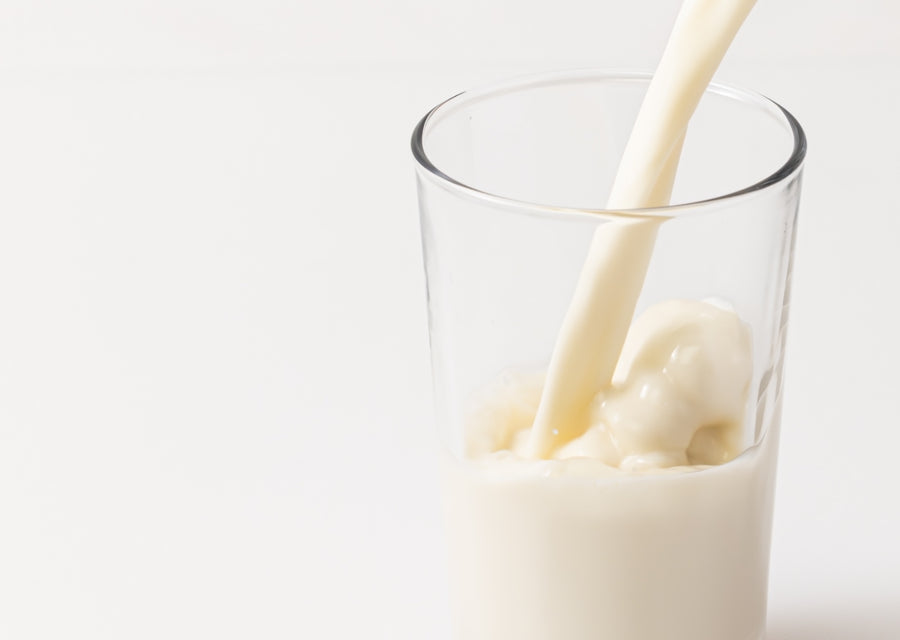 Glass of oatmilk being poured with a white background