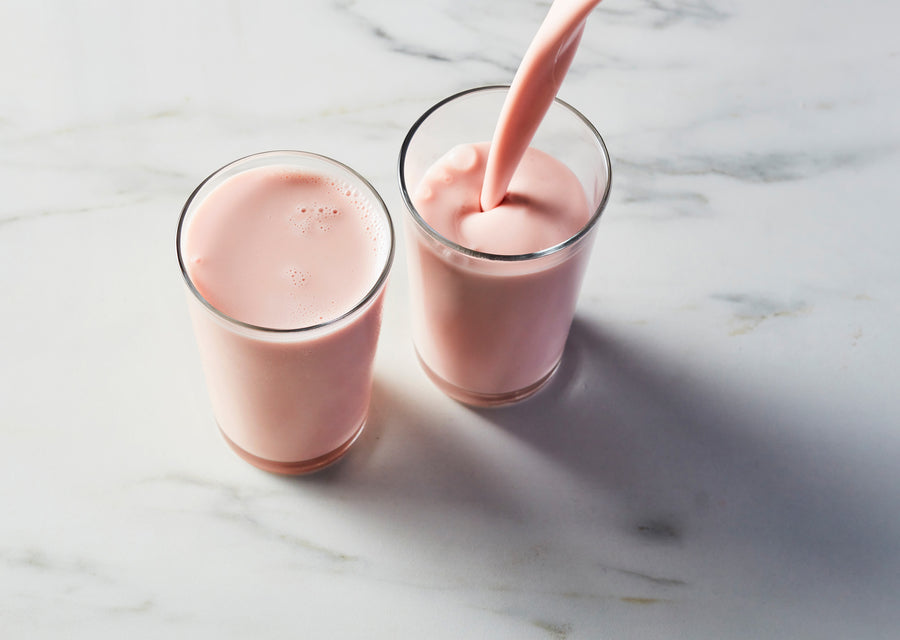 Strawberry kefir being poured into two glasses on a marble surface