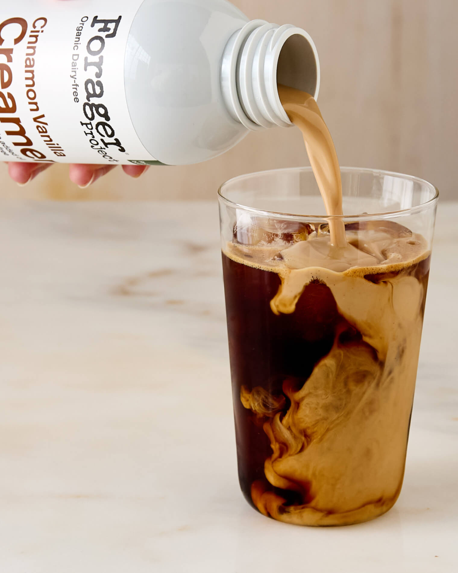 Forager Cinnamon Vanilla creamer being poured into a glass of iced coffee.