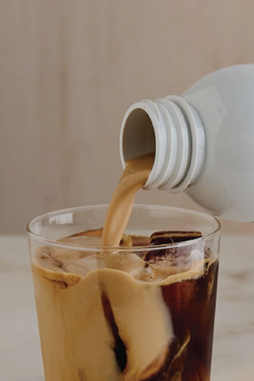 Creamer poured into a glass of iced coffee 
