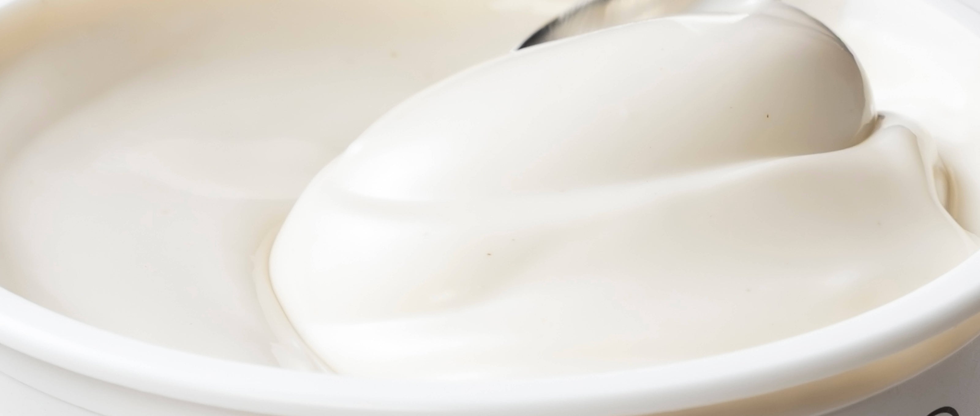 Close-up of a spoon dipping into a bowl of white yogurt.