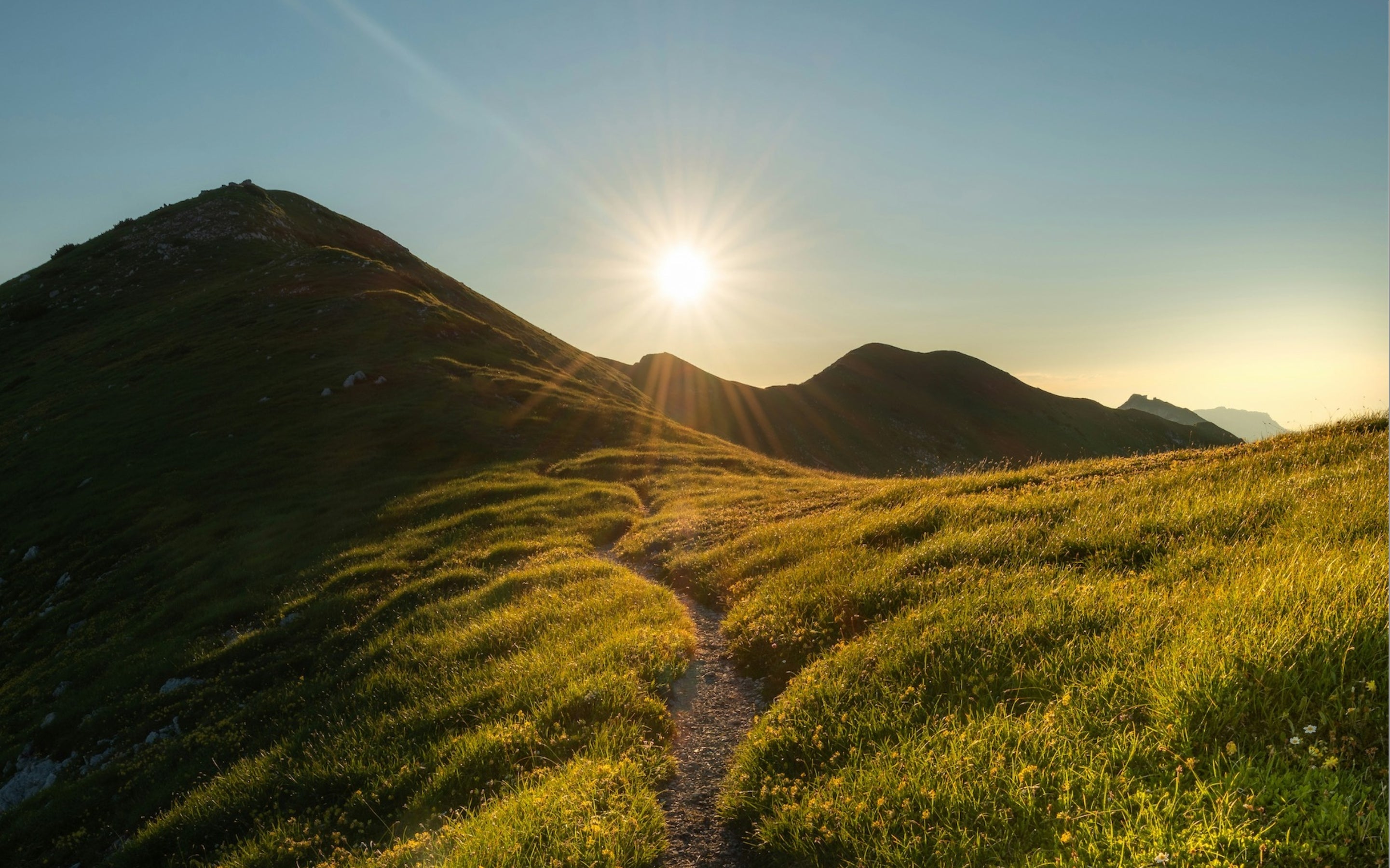 Sunrise over a mountain landscape with a path leading towards the sun.