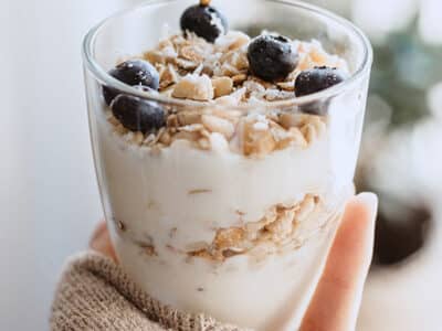 Yogurt parfait with granola and blueberries held in woman's hand.