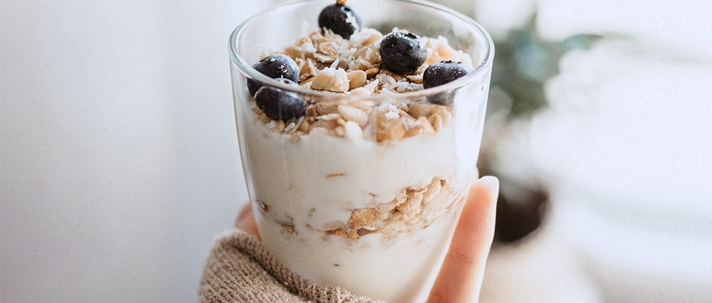 Yogurt parfait with granola and blueberries held in woman's hand.