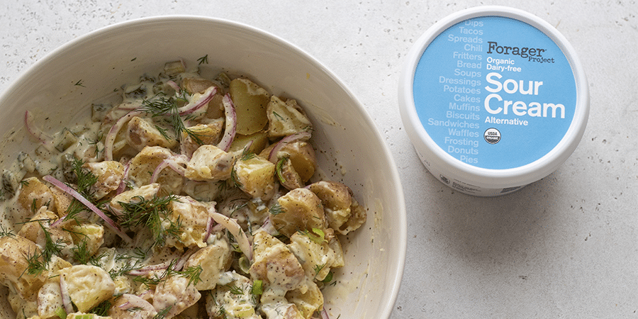 A bowl of creamy vegan dill pickle potato salad next to a tub of Forager Project Sour Cream.