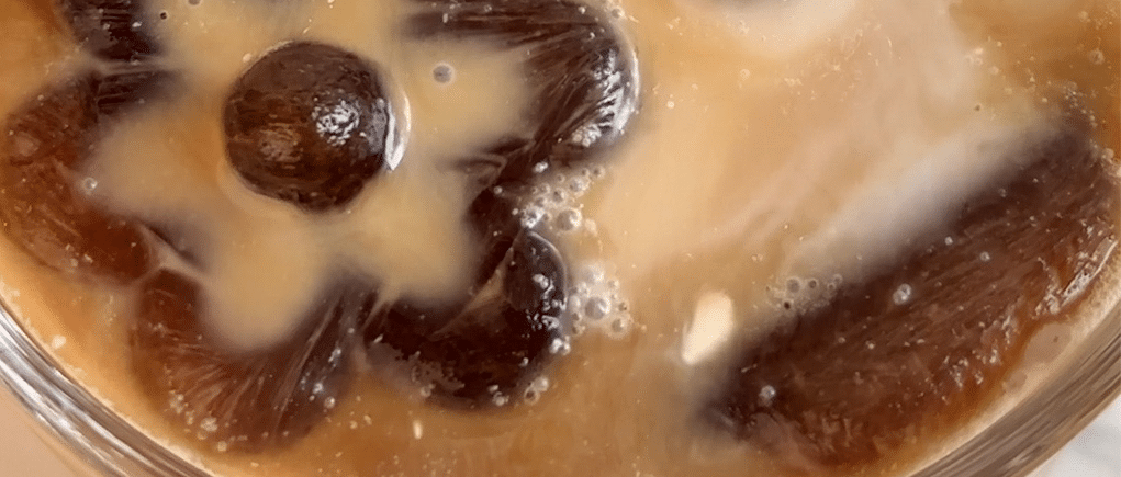 Extreme close up of a glass of dairy-free iced coffee with flower shaped ice cubes.