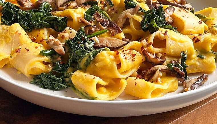 Close up of butternut squash pasta with sauteed kale and mushrooms