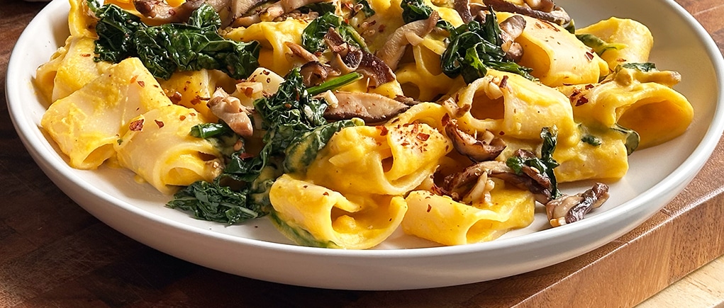 Close up of butternut squash pasta with sauteed kale and mushrooms